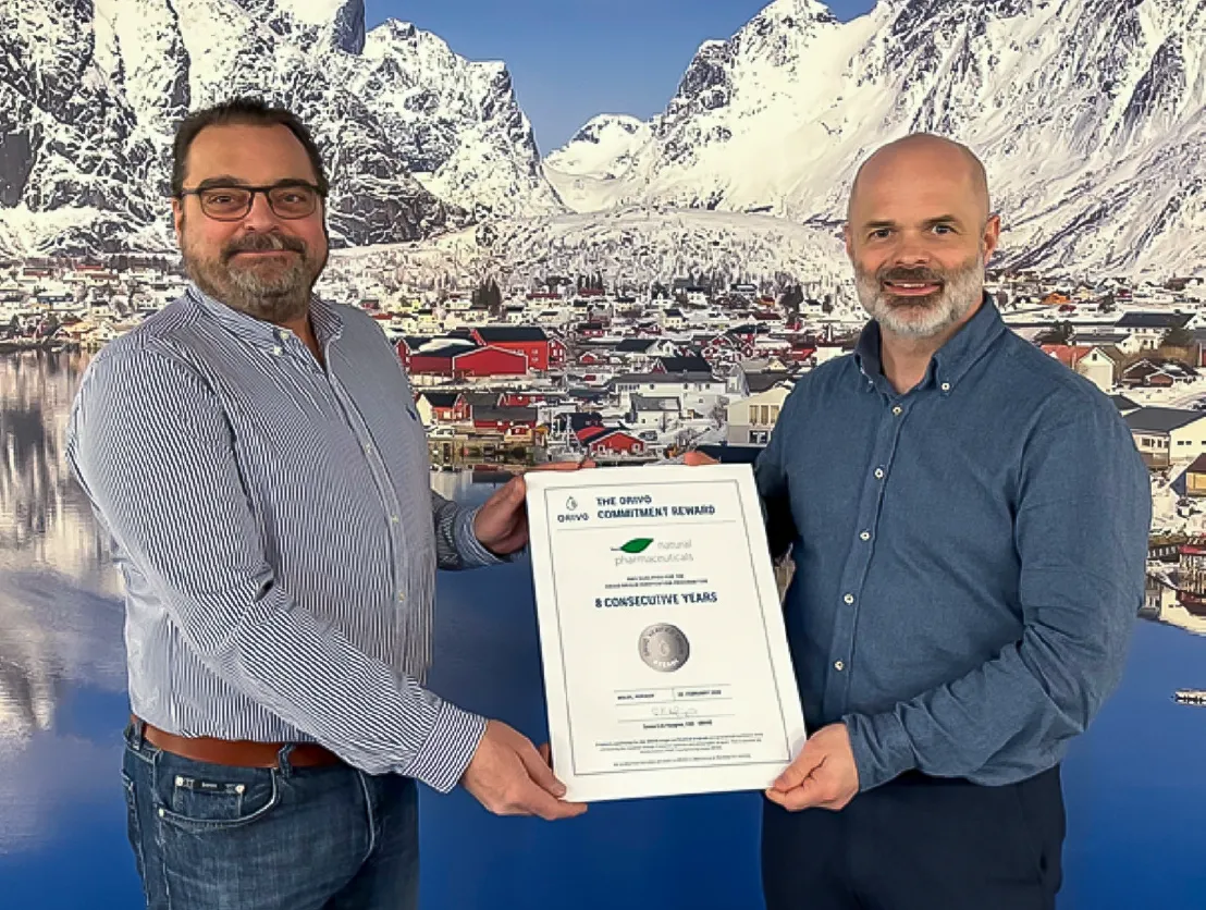 Natural Pharmaceuticals OmegaMarine™ Premium 
                            Dwóch mężczyzn trzyma wspólnie certyfikat ORIVO (wyróżnienie za wieloletnie zaangażowanie); 
                            w tle zimowy pejzaż miasteczka nad wodą i ośnieżone góry.
                        